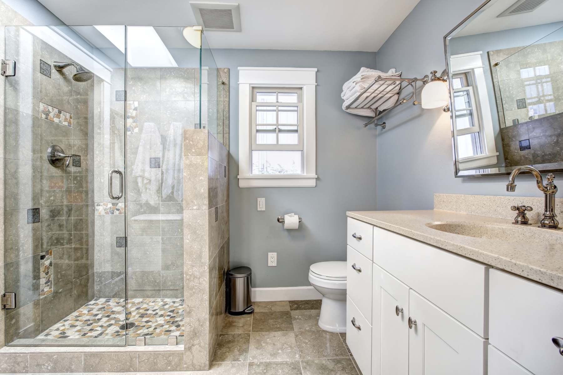 Light blue modern bathroom interior with glass door shower and white cabinet with  mirror